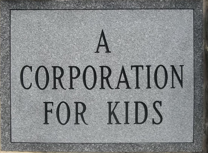 A sign on a brick wall that says a corporation for kids