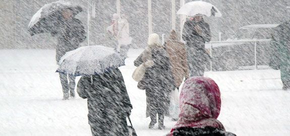 A group of people walking in the snow with umbrellas.