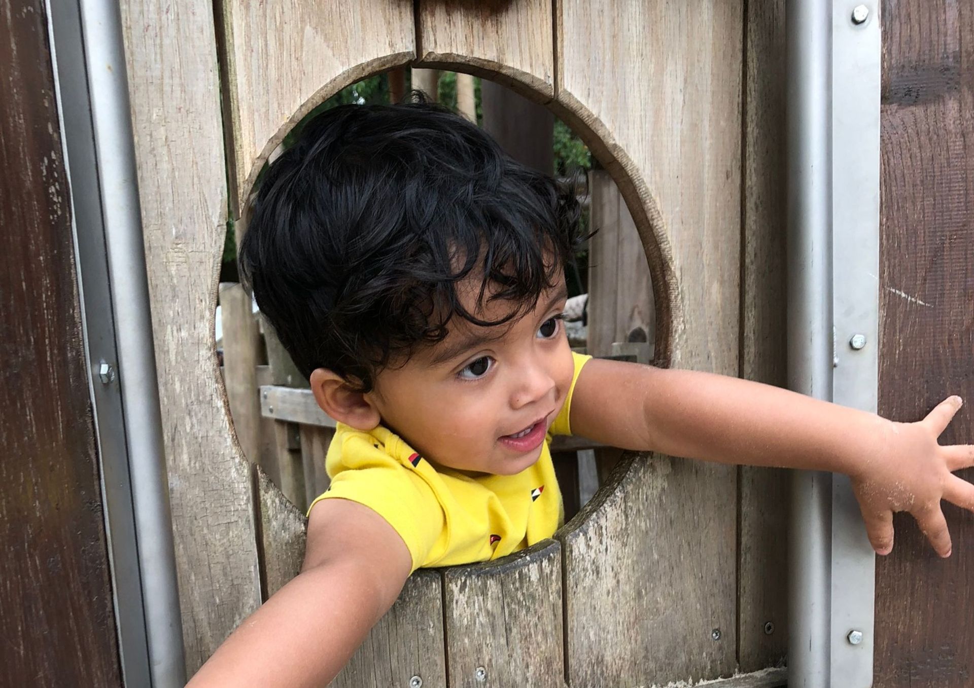 Een jongetje kijkt uit een gat in een houten constructie.