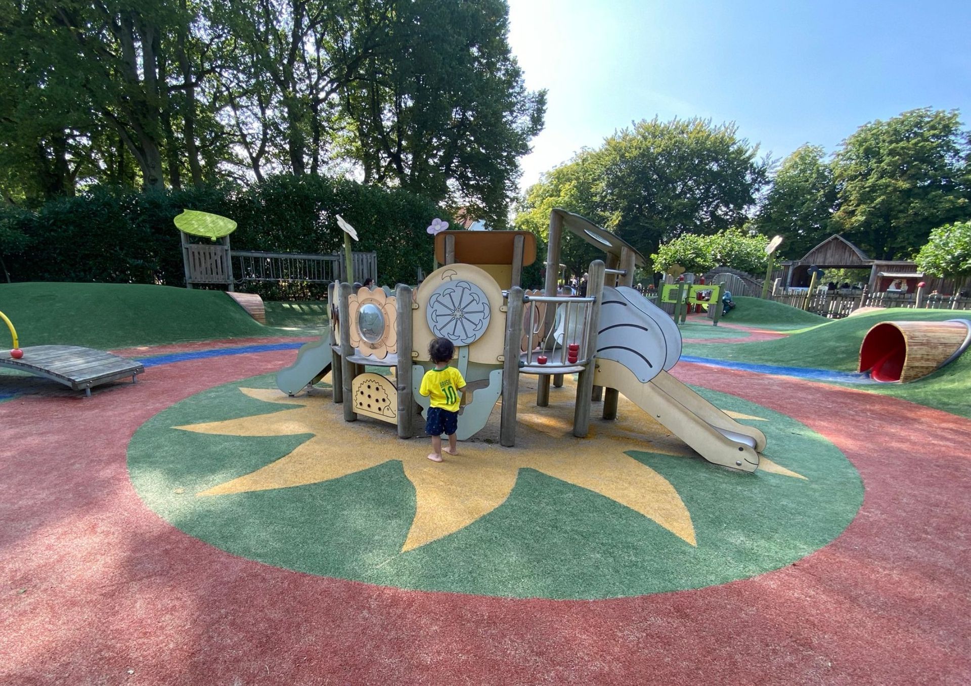 Een jongetje staat voor een speeltuin in een park.