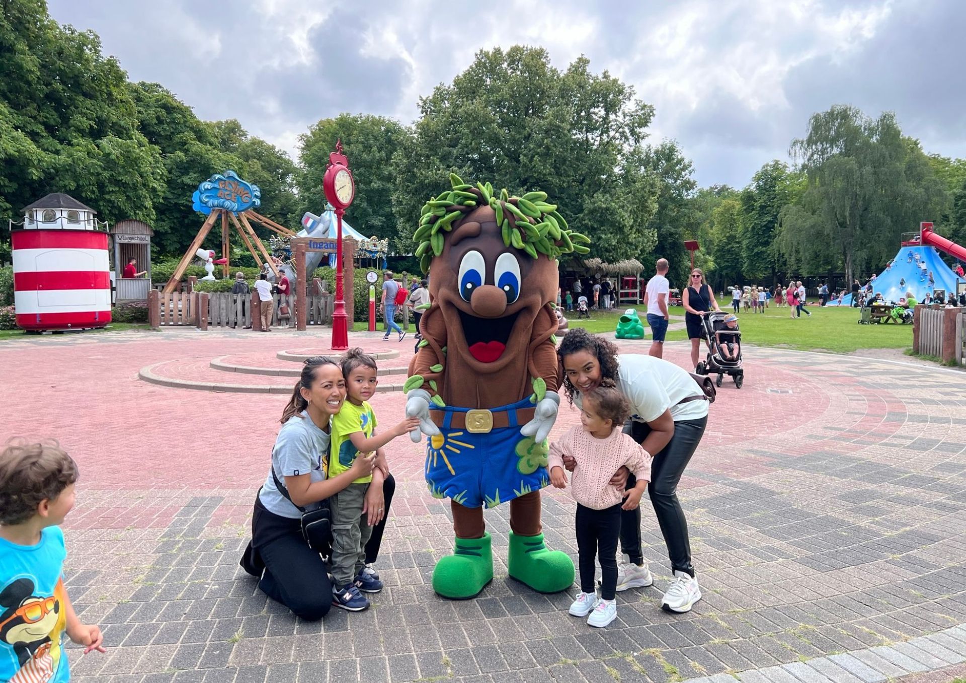 Een groep mensen poseert voor een foto met een mascotte in een park.