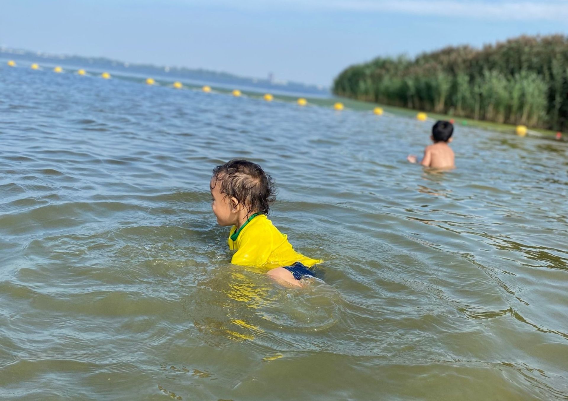 Een jongen in een geel shirt zwemt in een meer.