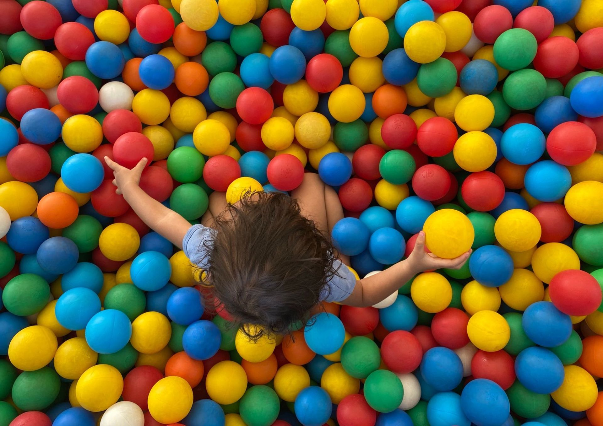 Een klein meisje speelt in een ballenbak vol met gekleurde ballen.