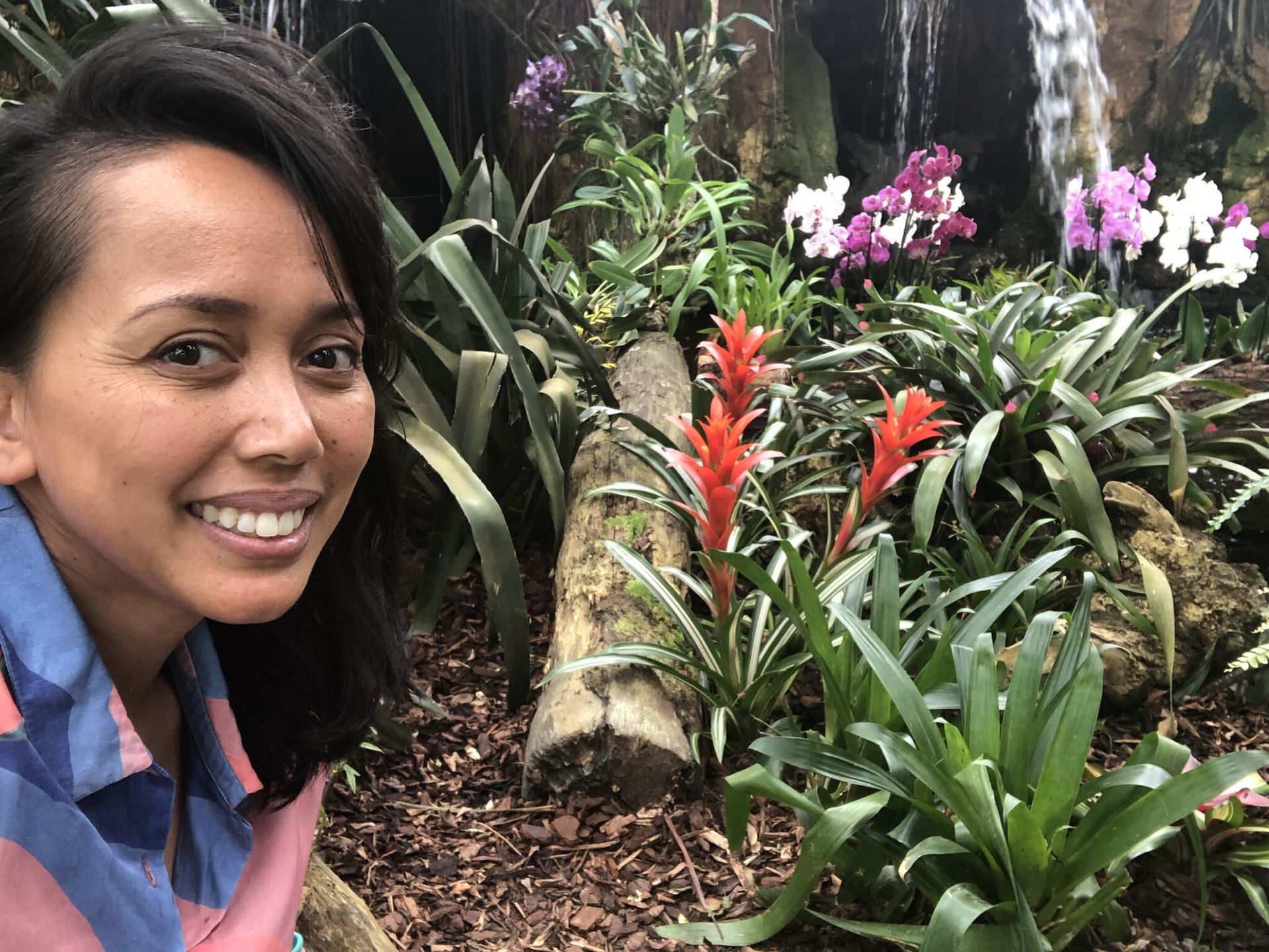 Een vrouw lacht voor een waterval en bloemen.