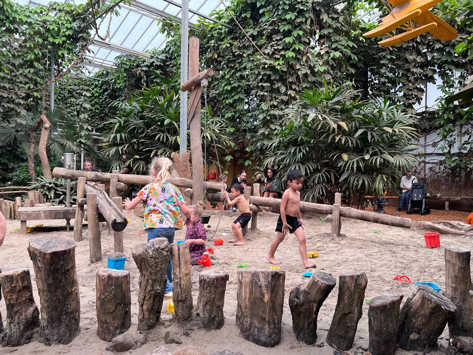 Een groep kinderen speelt in een zandbak gemaakt van boomstronken.