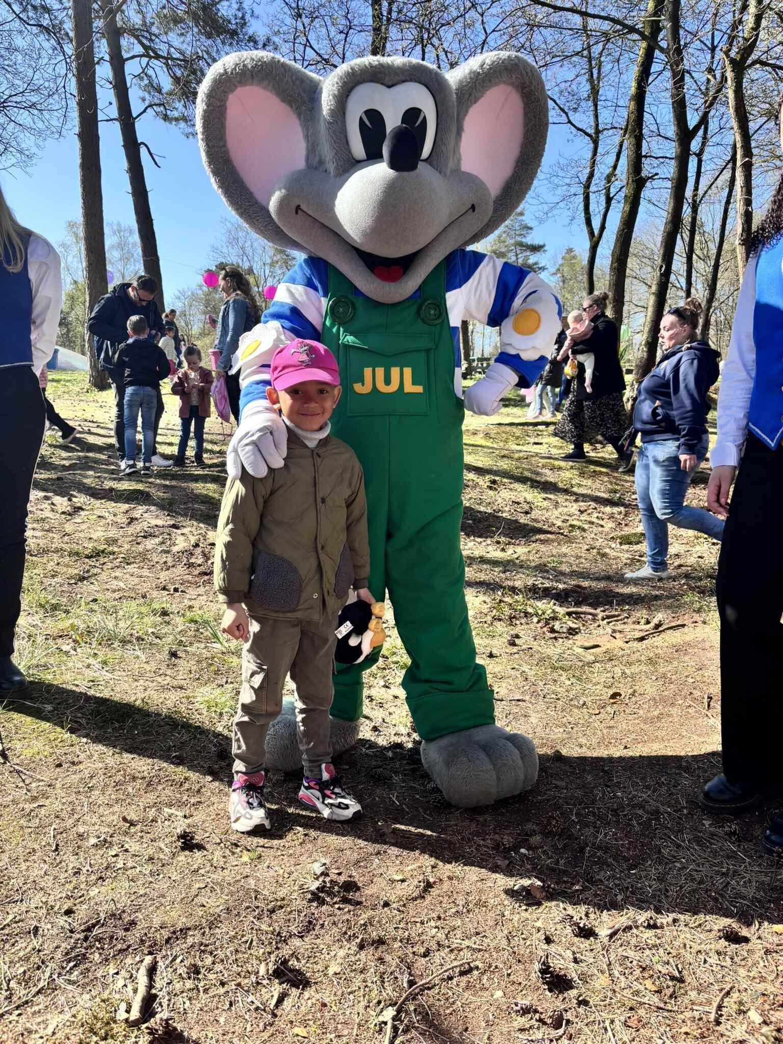 Een klein meisje staat naast een mascotte in een park.