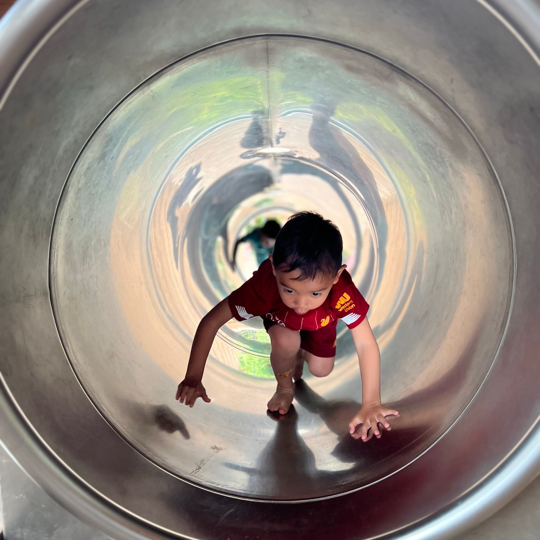 Een jonge jongen in een rood shirt gaat van een metalen glijbaan