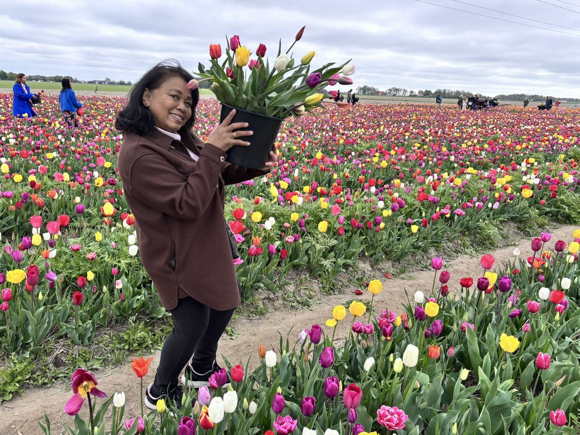 Een vrouw houdt een pot met bloemen vast in een veld met tulpen.