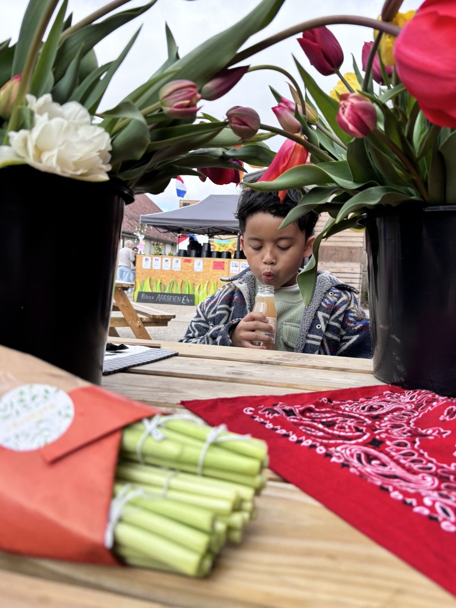 Een jonge jongen drinkt uit een kopje terwijl hij aan een tafel zit met bloemen in potten.