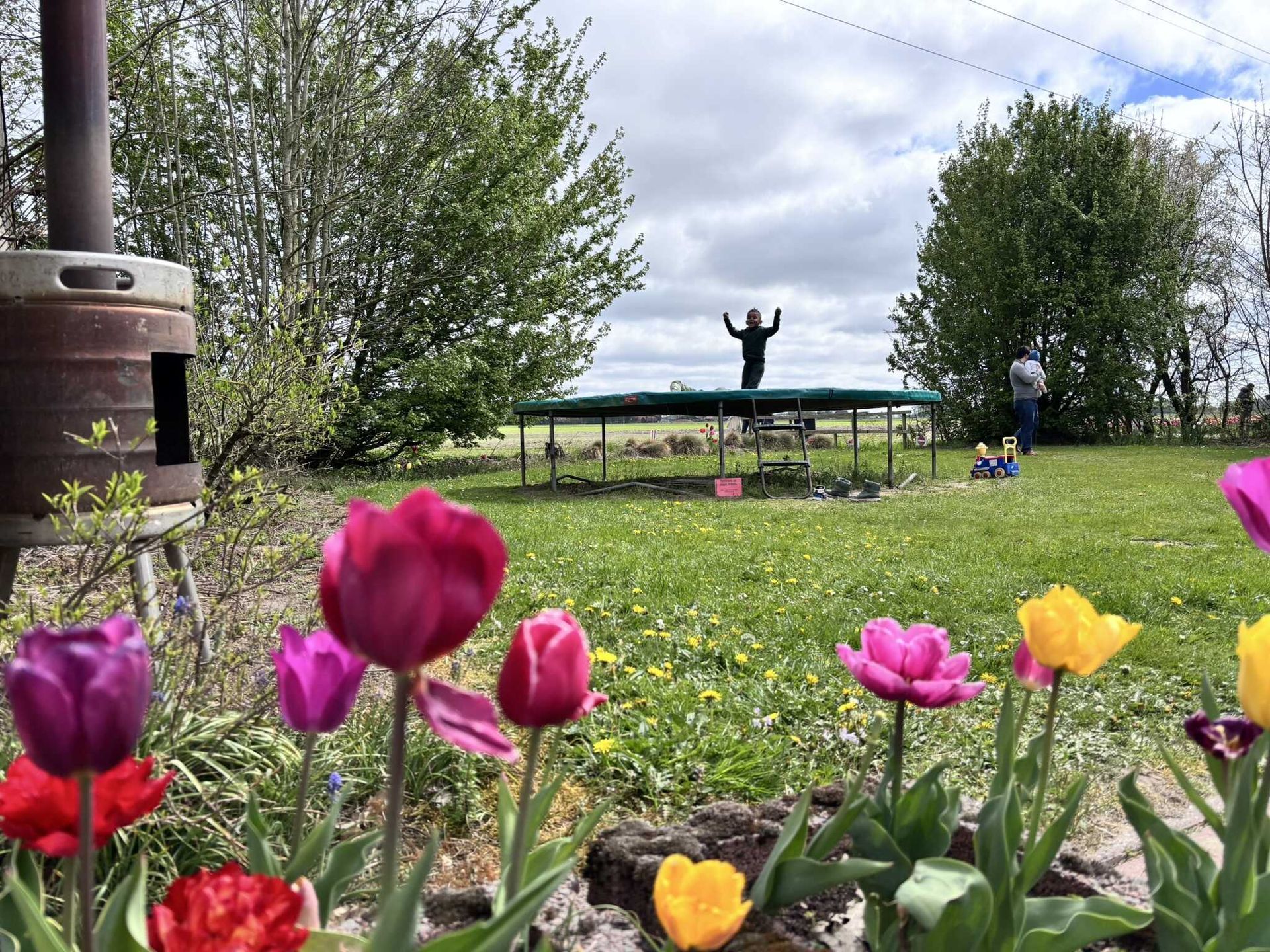 Een persoon springt op een trampoline in een veld met bloemen op de voorgrond.