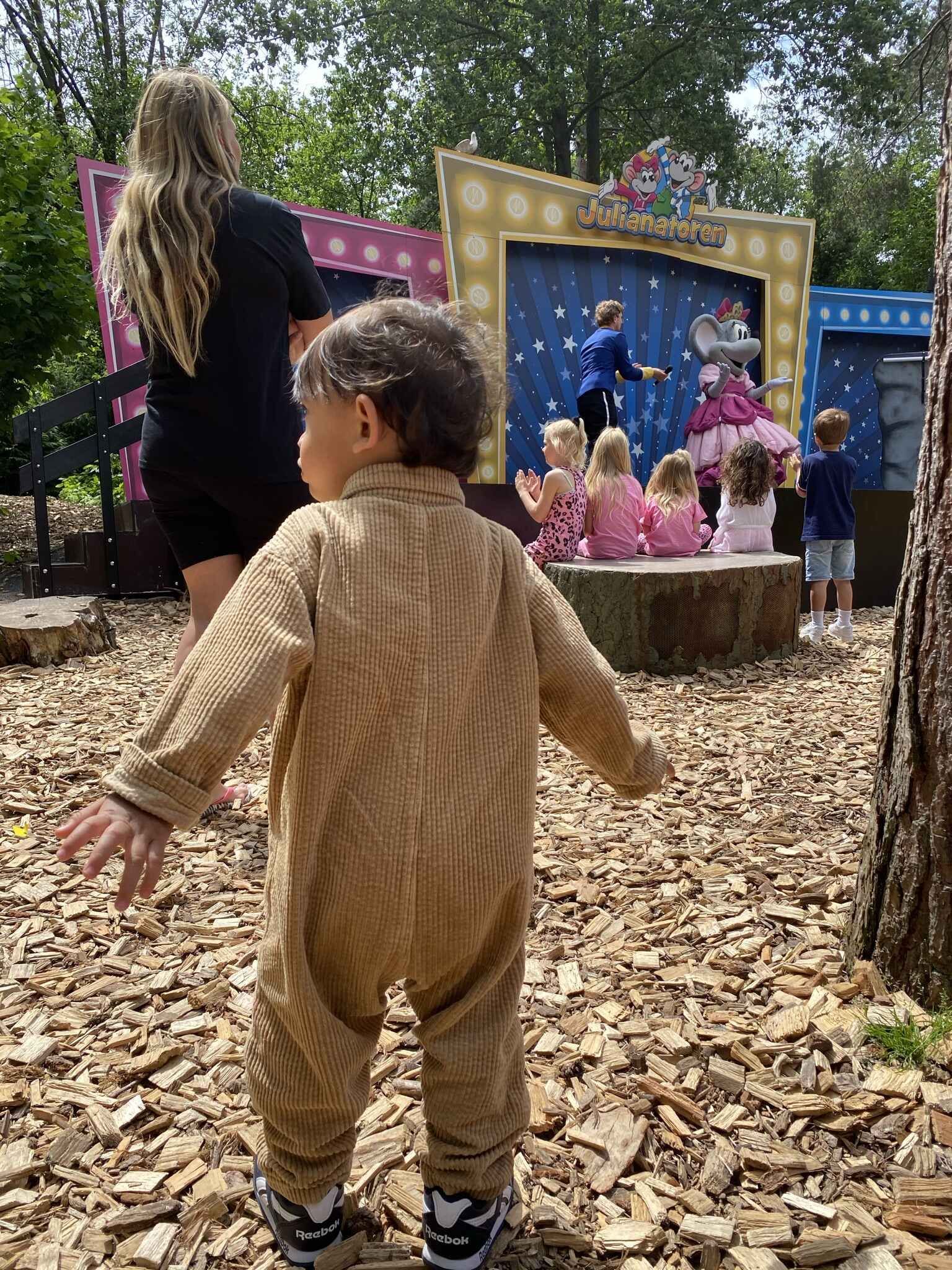 Een klein jongetje in een kostuum staat in het vuil voor een podium.