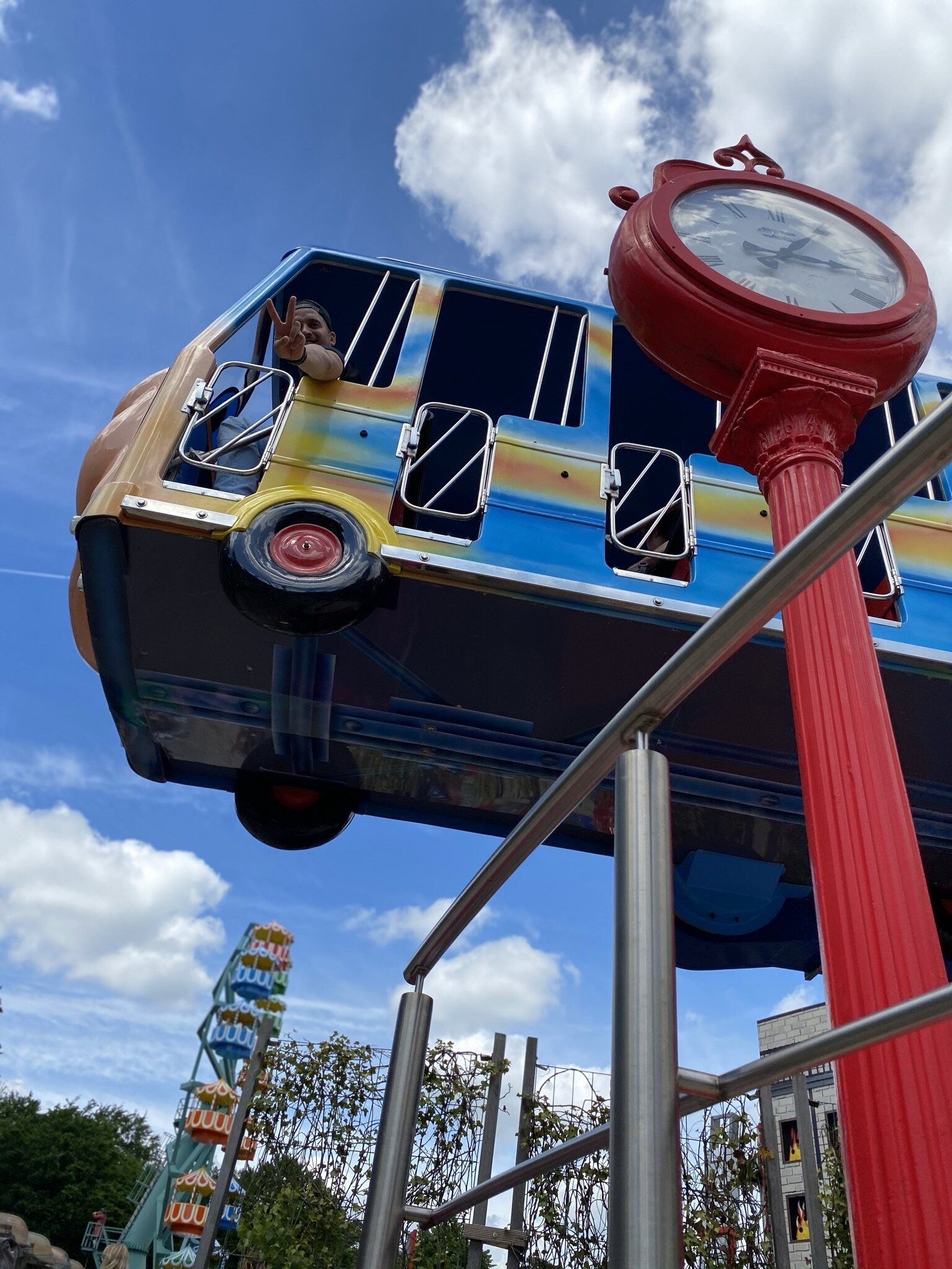 Een kleurrijke bus hangt aan een rode paal naast een klok.