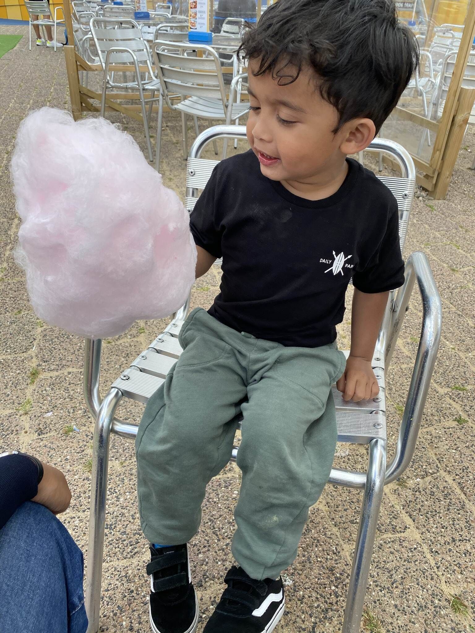 Een jongetje zit op een stoel en eet suikerspin.