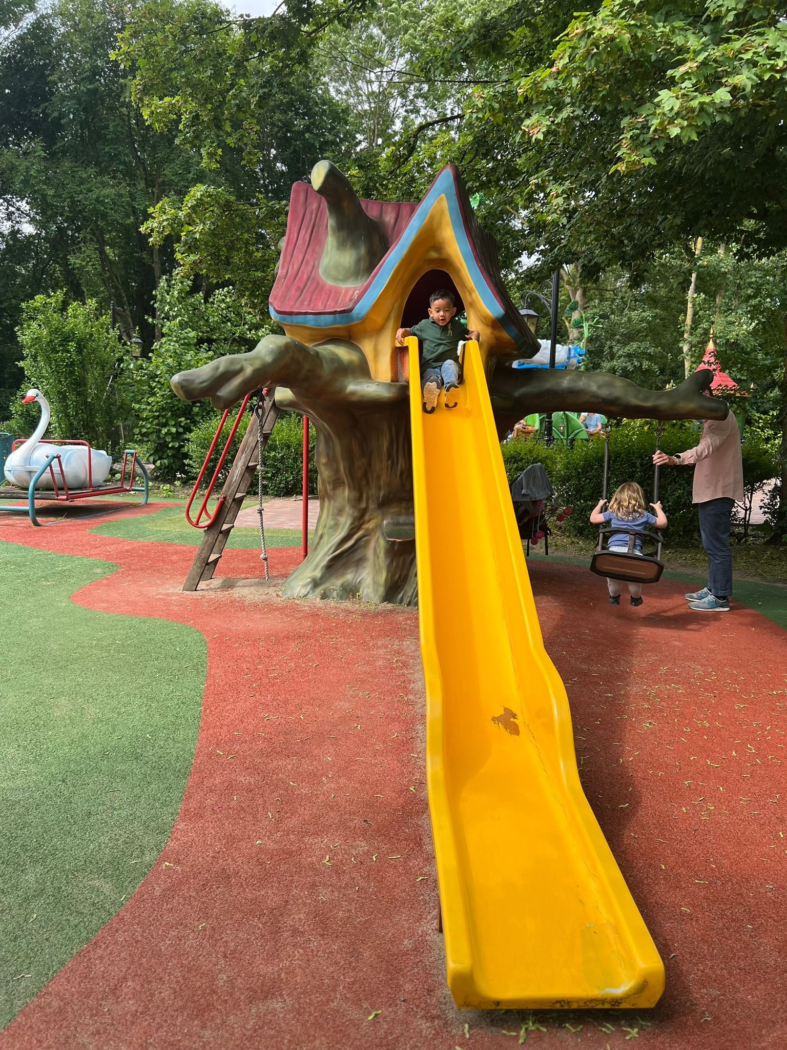 Een kind glijdt op een gele glijbaan in een speeltuin.