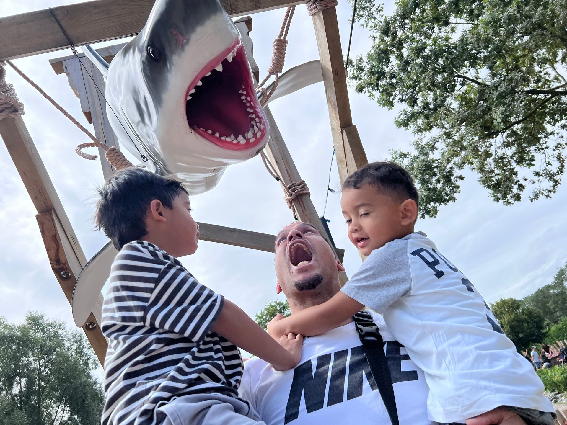 Een man en twee kinderen spelen met een haaienbeeld.