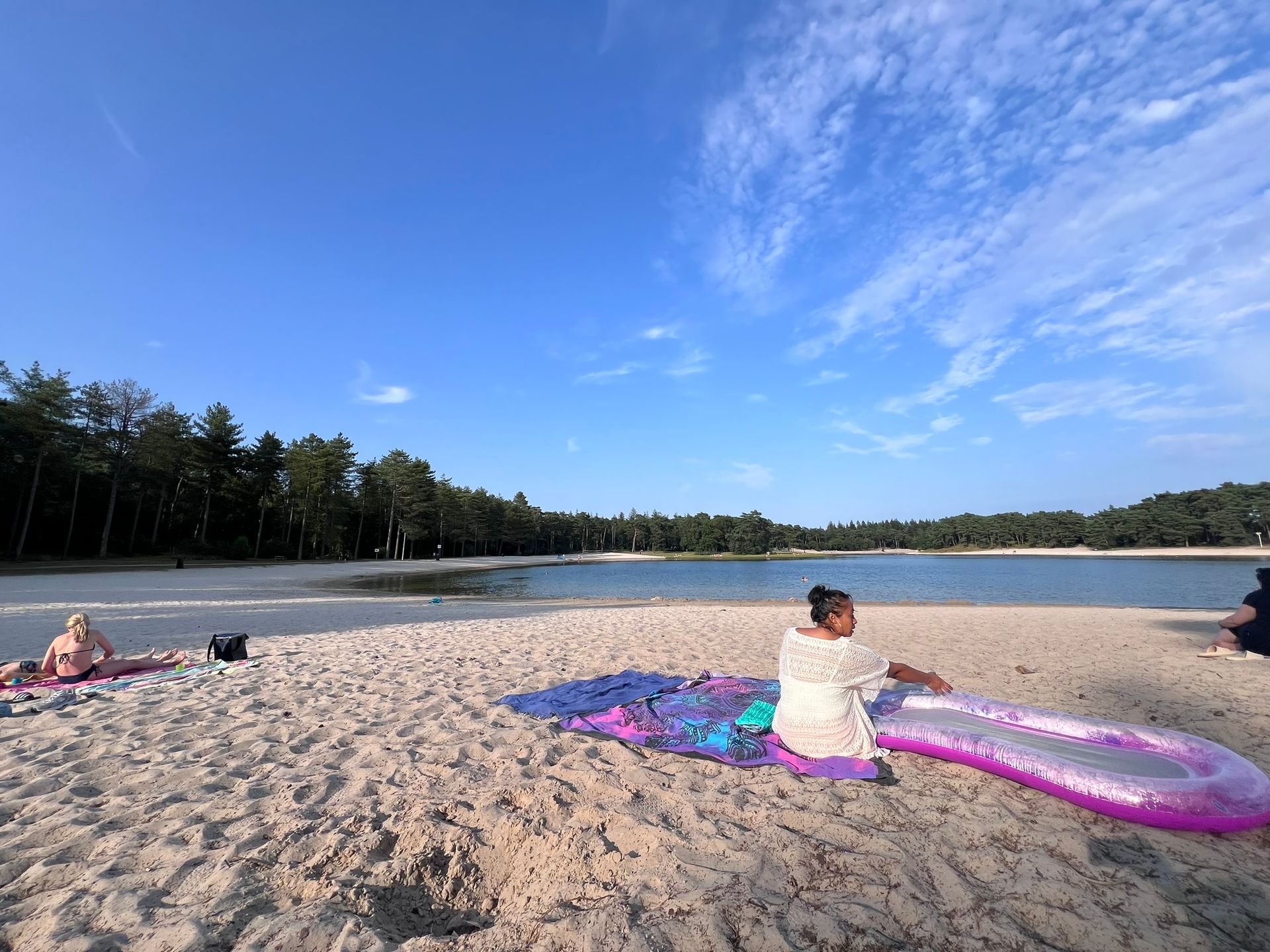 Een vrouw zit op een deken op het strand bij een meer.