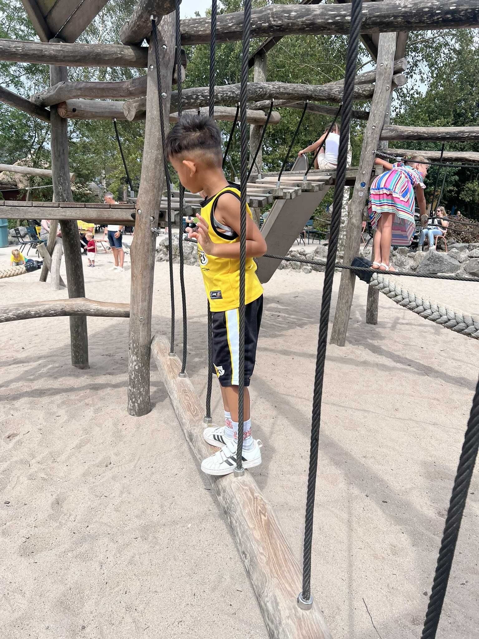 Een jonge jongen staat op een touwbrug bij een speeltuin.