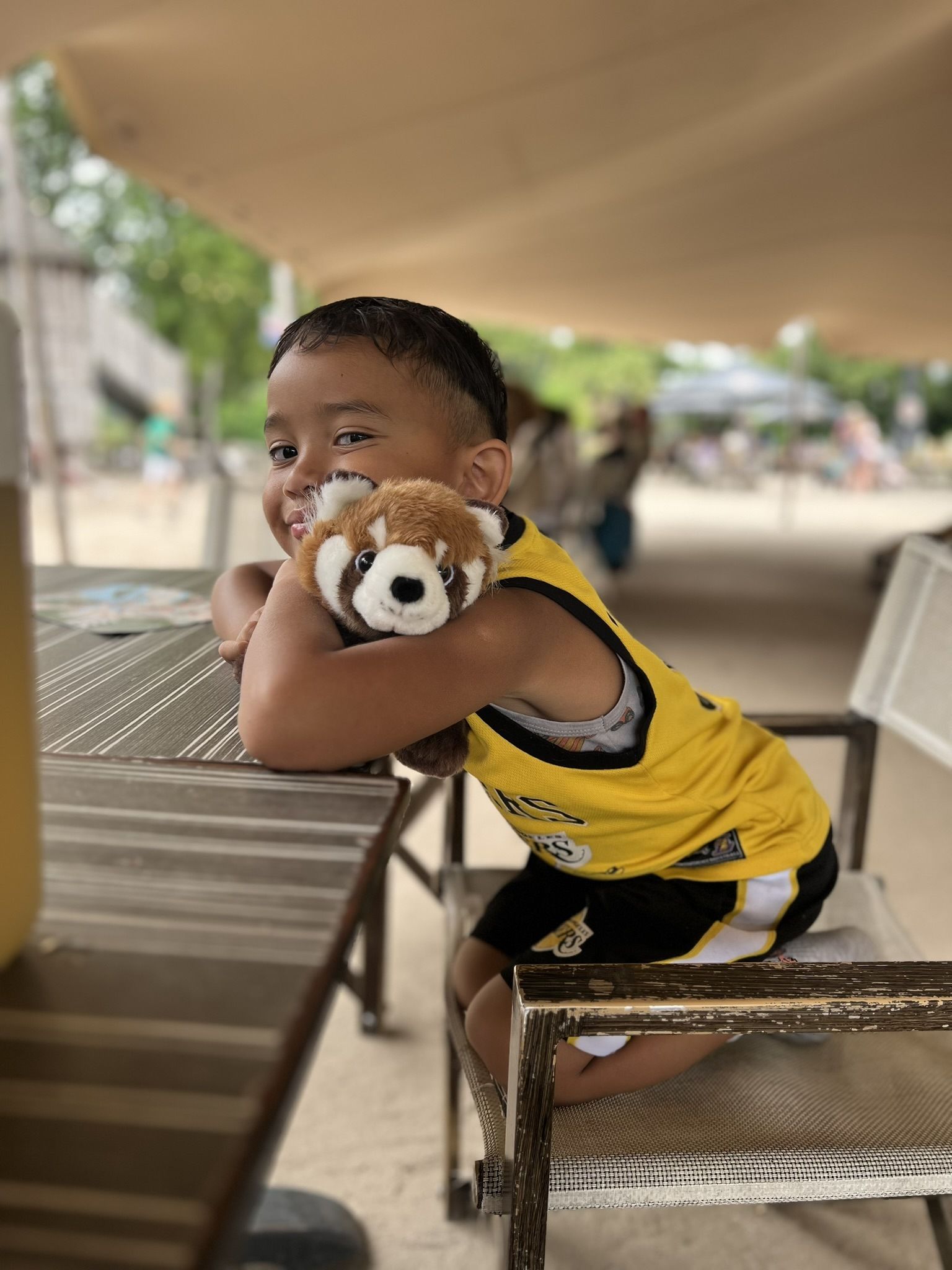 Een jonge jongen zit aan een tafel met een knuffeldier in zijn handen.