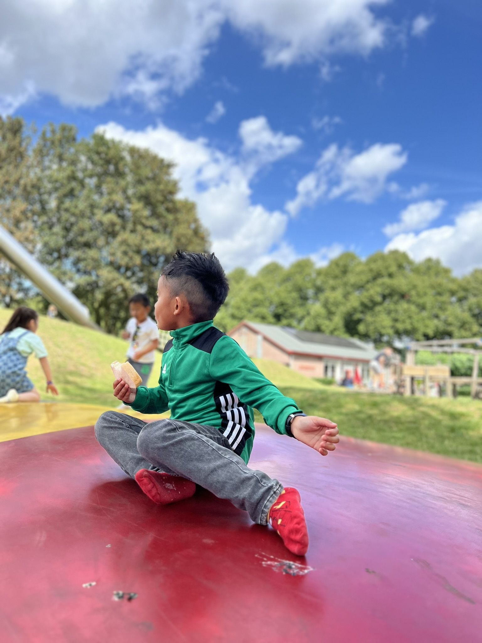 Een jonge jongen zit op een rood kussen in een park.