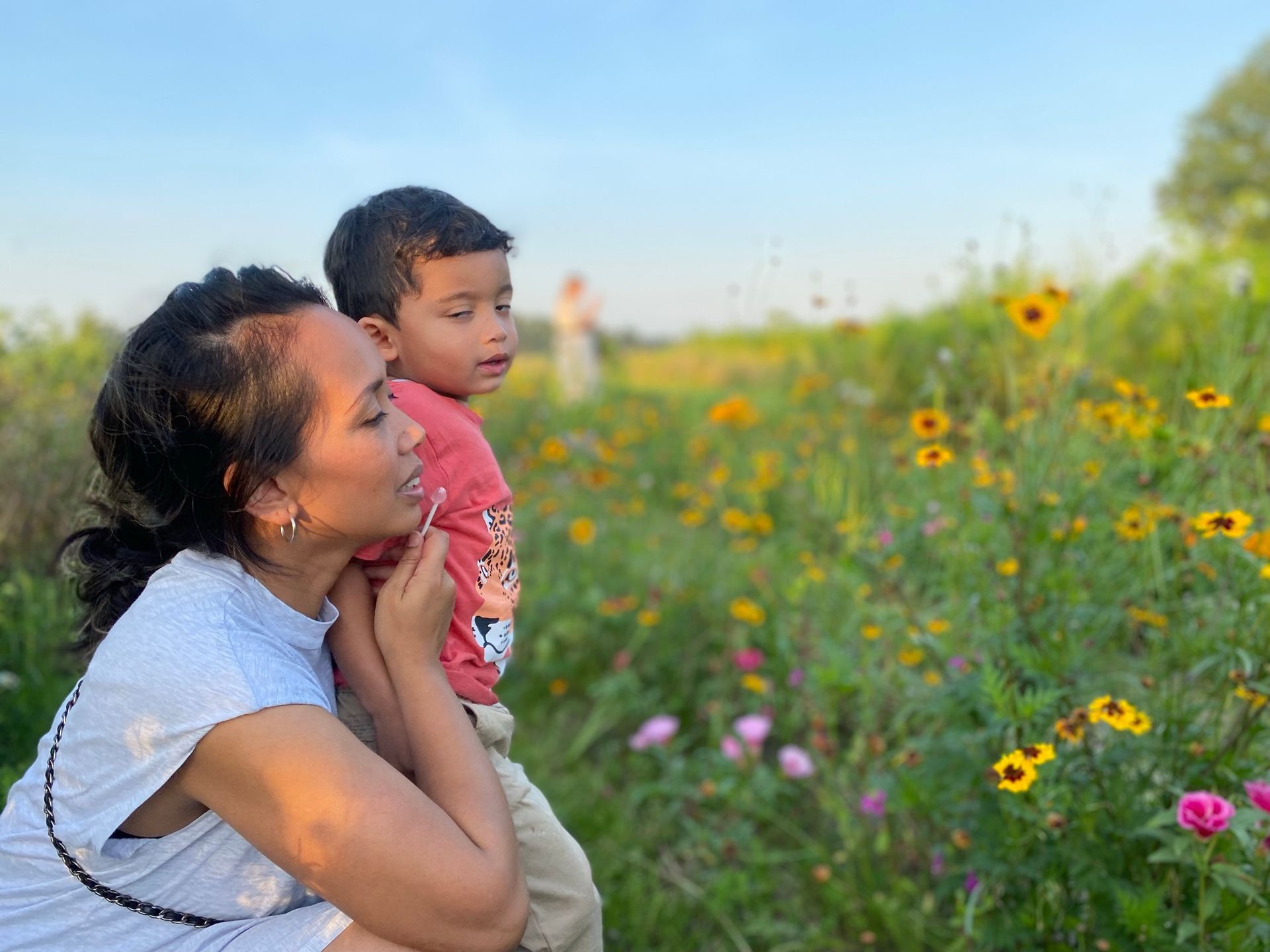 Een vrouw houdt een kind vast in een bloemenveld.