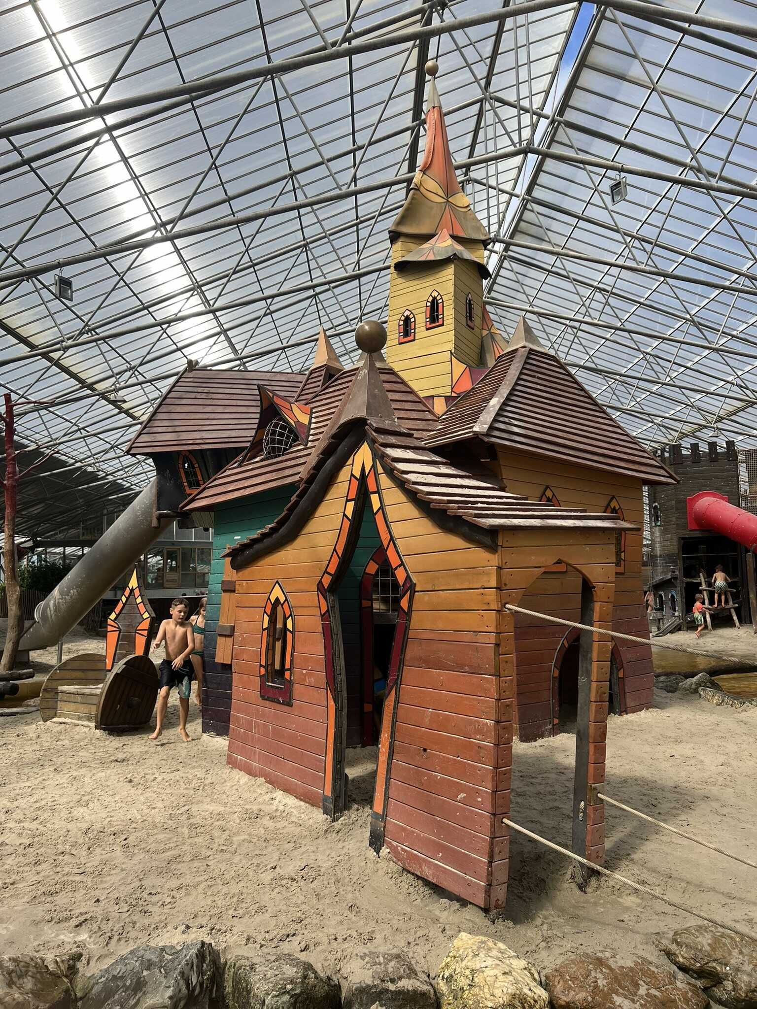 Een indoor strand met een houten huis en een glijbaan.