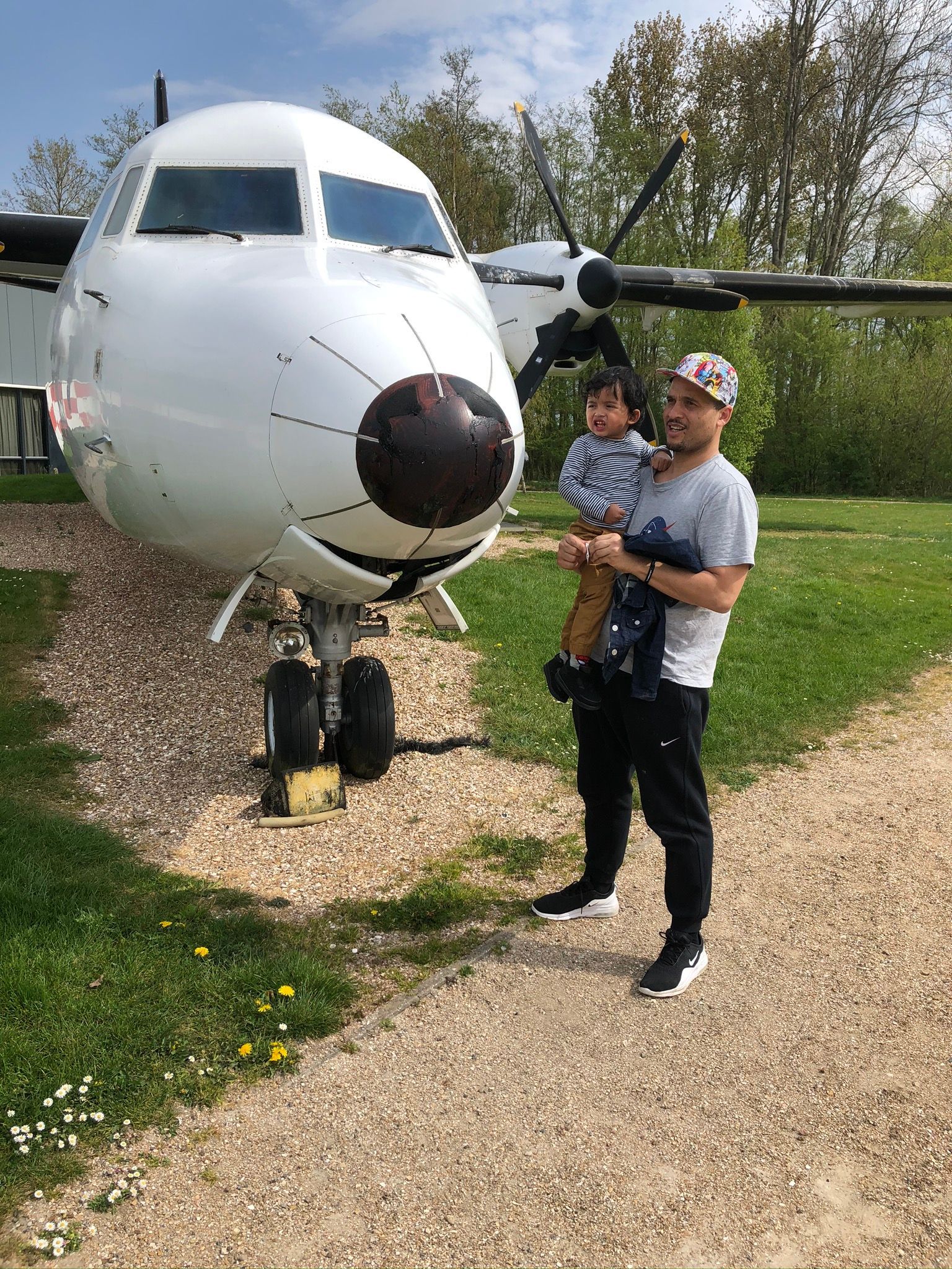 Een man houdt een baby vast voor een vliegtuig bij Aviodrome. 