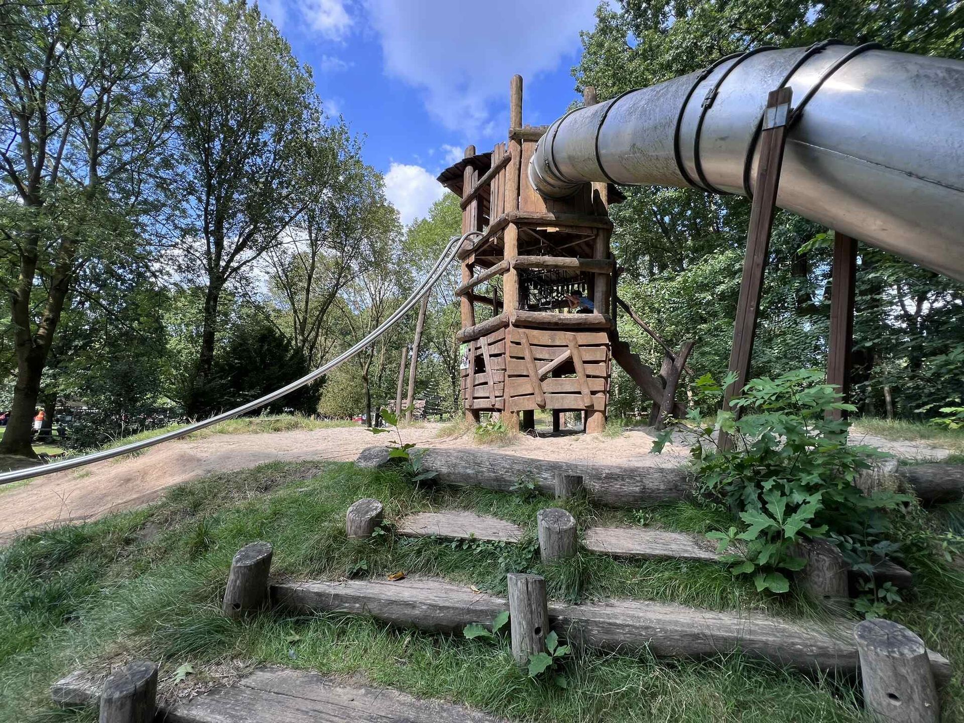Een houten speeltuin met glijbaan en trappen in een park.