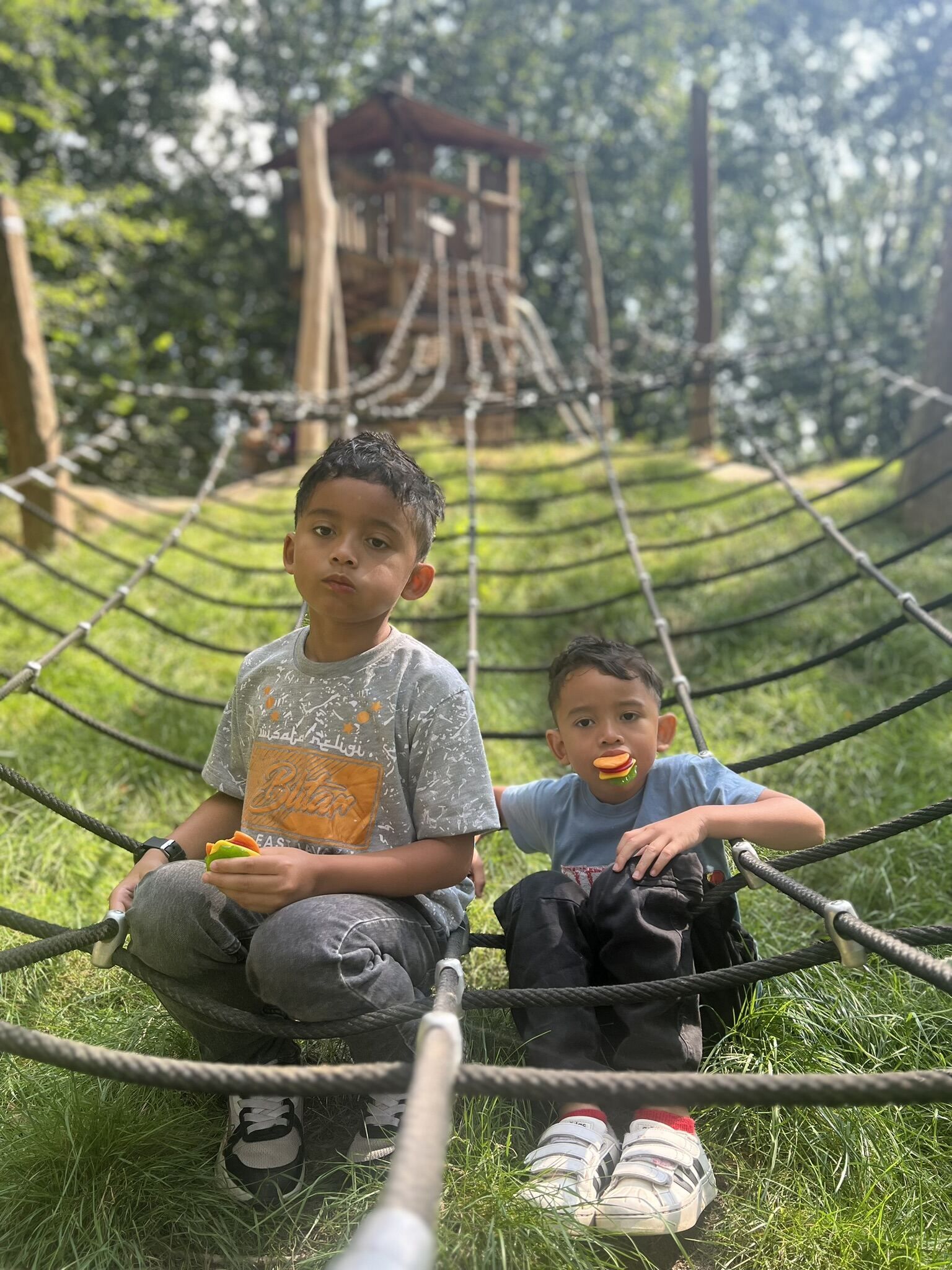 Twee jonge jongens zitten in een hangmat op een speelplaats.