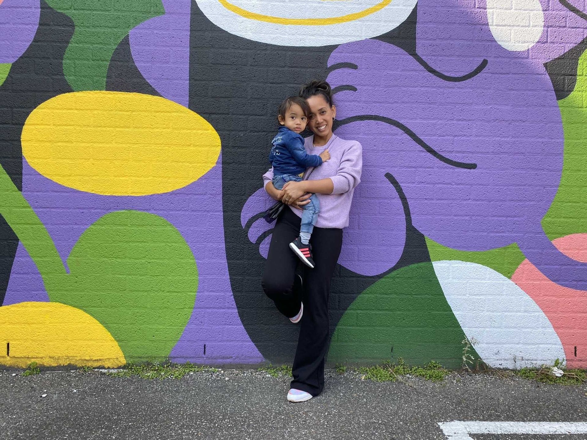 Een vrouw houdt een baby vast voor een kleurrijke muur.