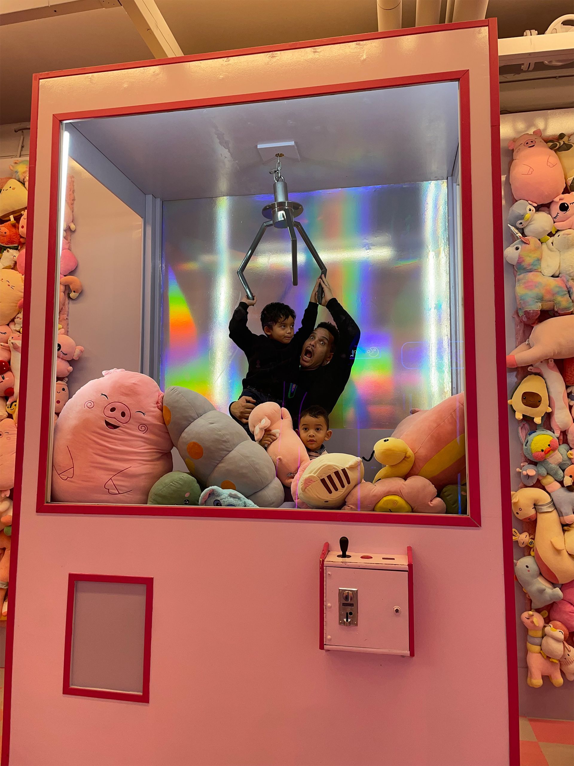 Twee kinderen spelen in een roze grijpmachine gevuld met knuffels.