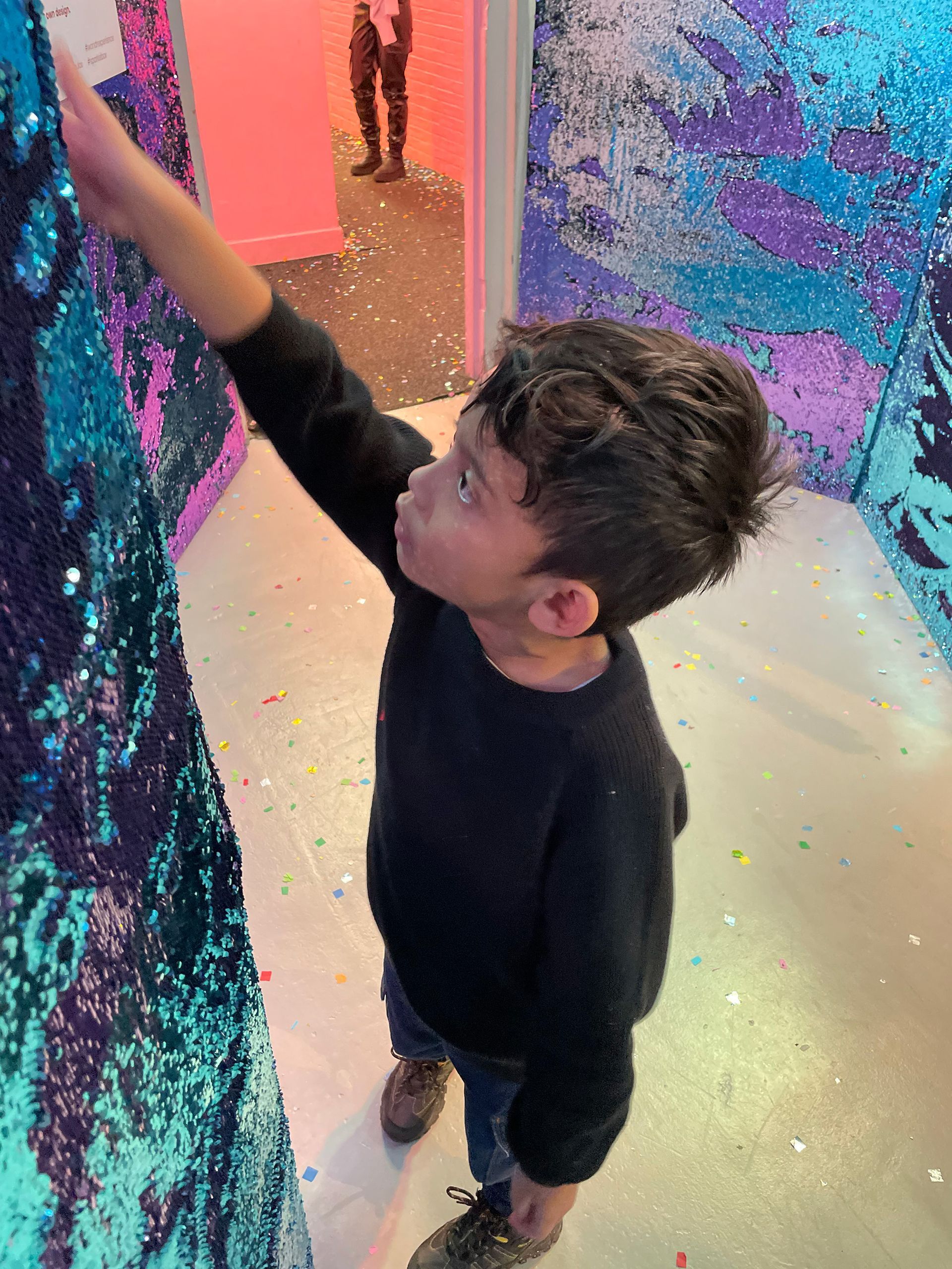 Een jonge jongen raakt een met pailletten bezette muur in een kamer aan.