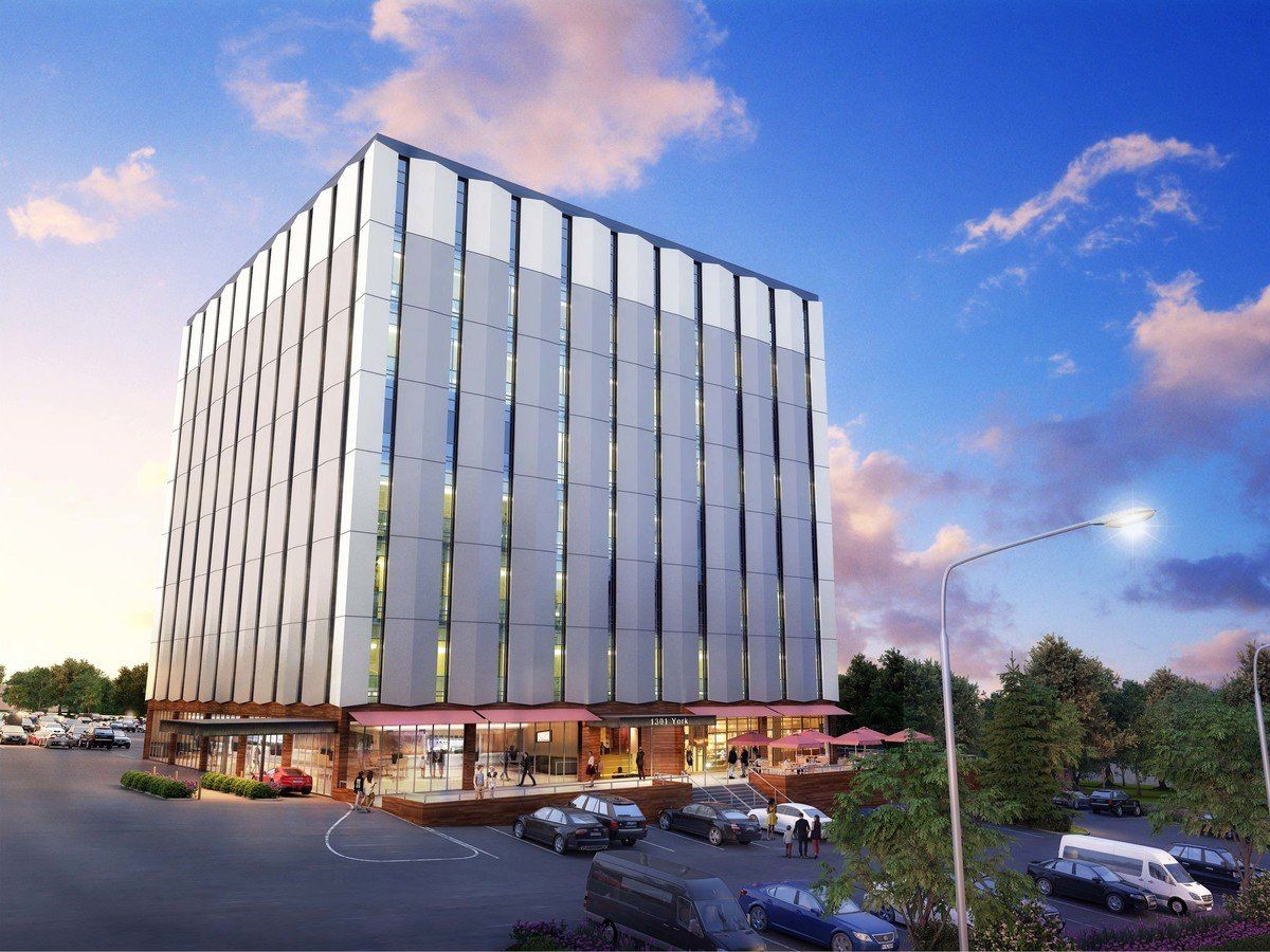 Modern office building with glass facade, parking lot, blue sky with clouds.