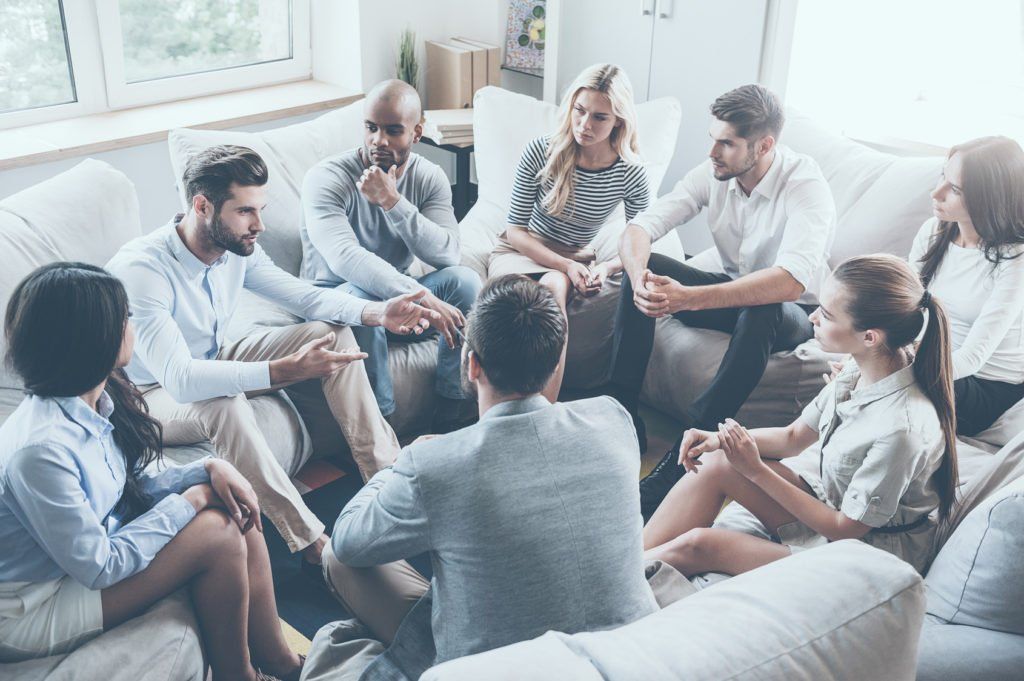 Group of diverse people sitting in a circle, talking in a casual setting.