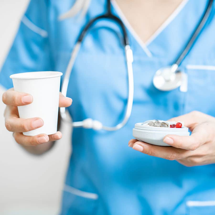 Nurse in blue scrubs holding a cup and a pill container with pills.