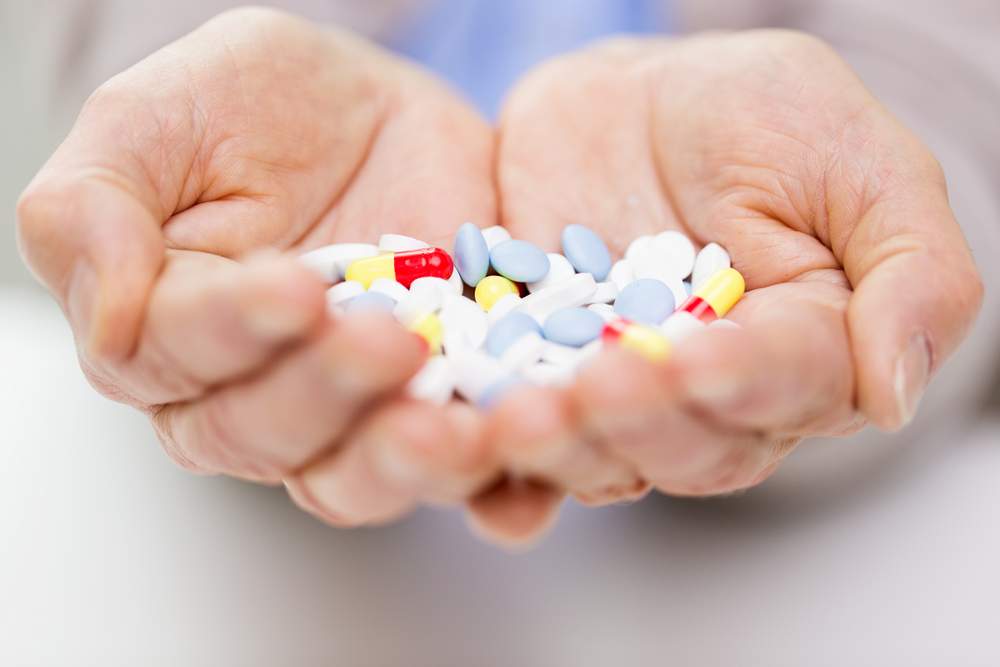 Hands cupped, holding a pile of various colorful pills.