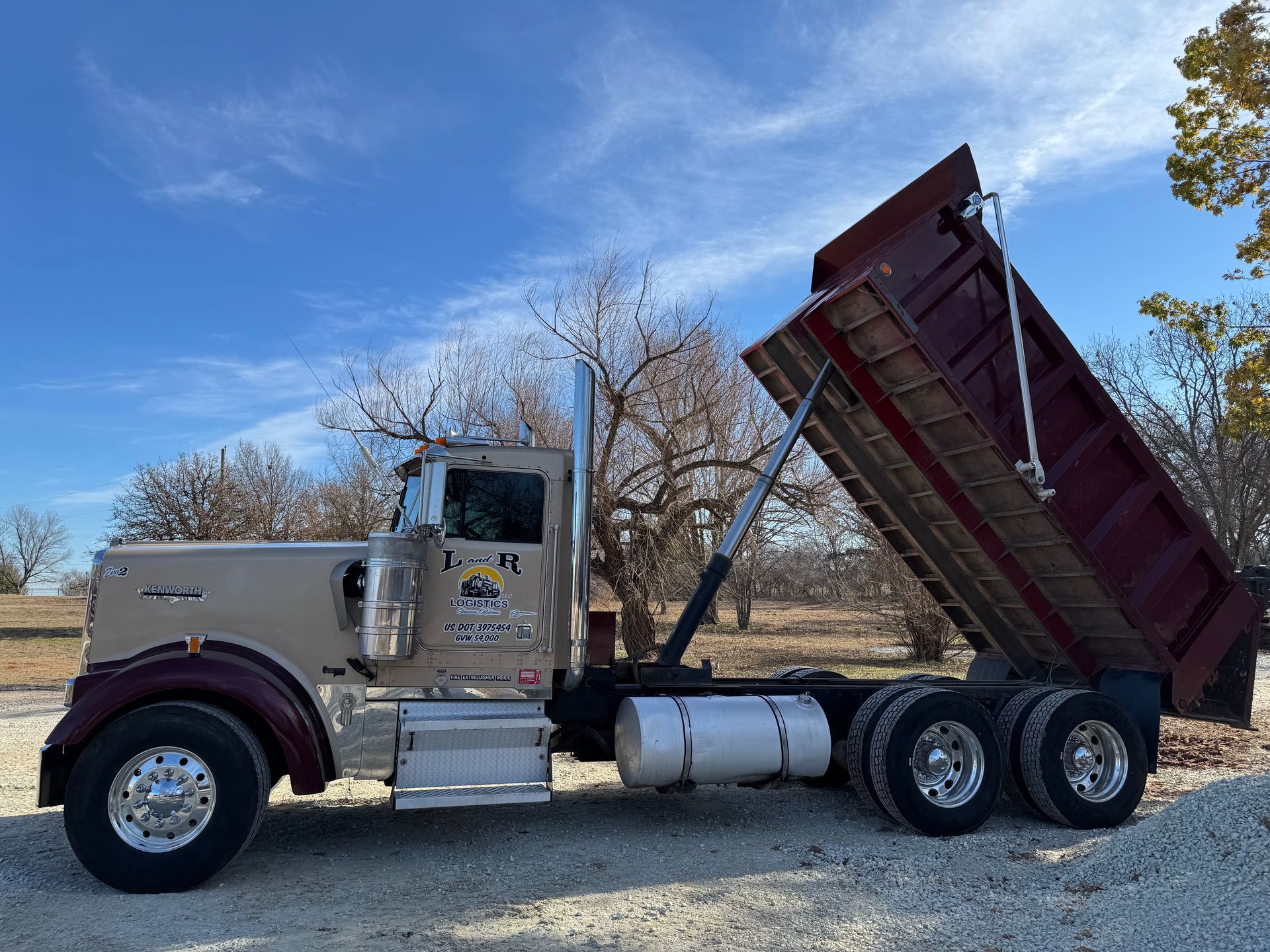 Bright red semi-truck with chrome accents driving on a road, blue sky background.