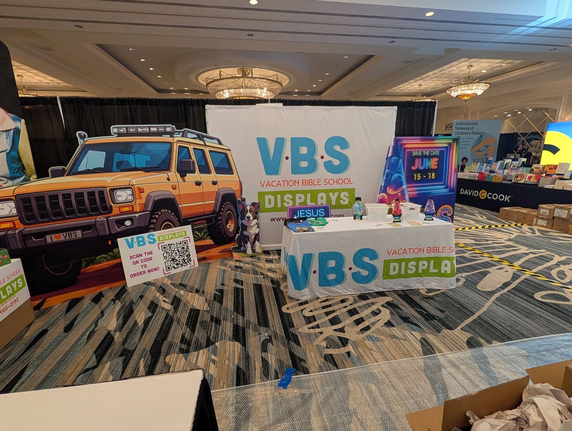 VBS trade show booth with car cutout, products on table, and a banner reading 