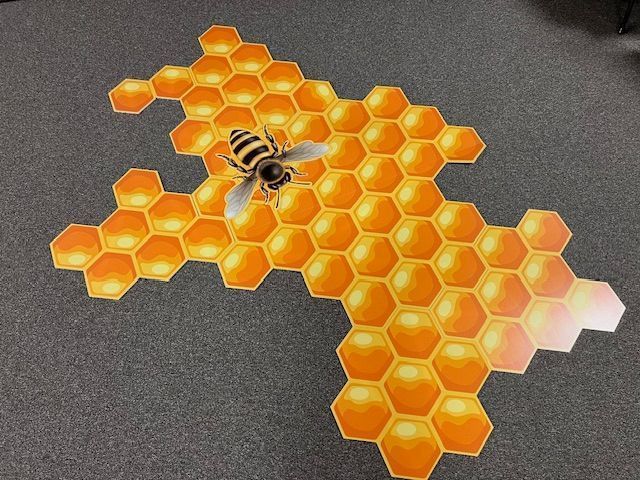 Bee on a honeycomb-shaped game board made of hexagonal tiles, orange and yellow, on a dark surface.