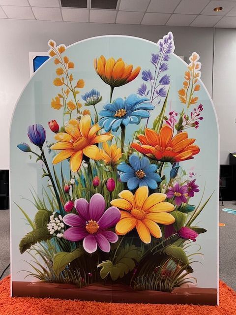 Cardboard cutout of colorful flowers in an arch shape, set on an orange surface.