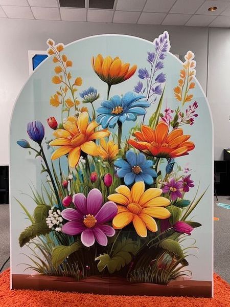 Colorful flower display with daisies and other blooms on a pale blue background.