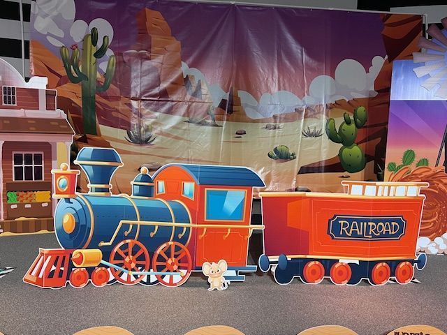 Cartoon train and backdrop of a desert scene. A small mouse stands near the train on the ground.