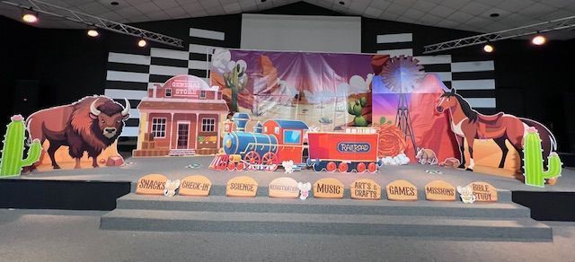 Stage set with a wild west theme: buffalo, train, desert background, town facade, and signs.