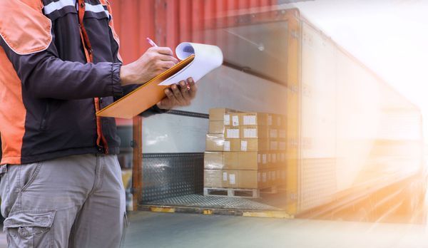 Delivery worker in orange vest, checking a clipboard next to a loading dock and boxes.