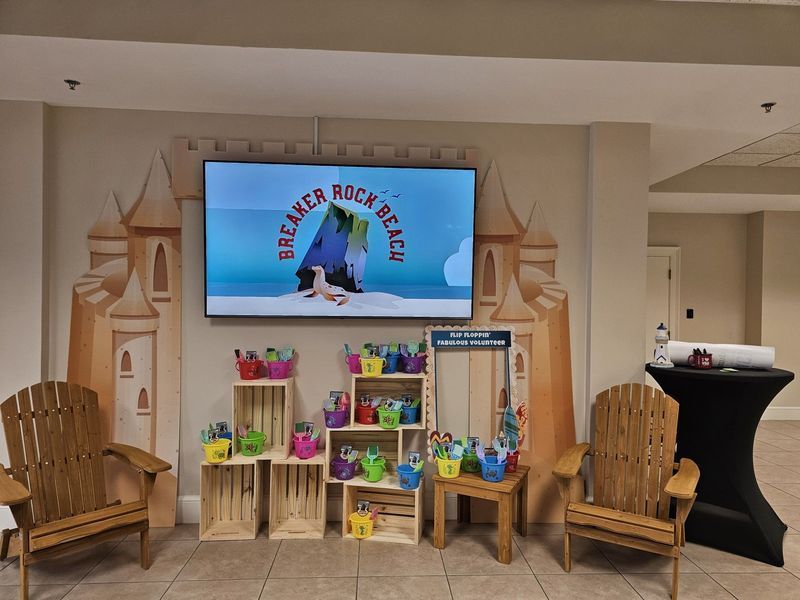 Event display with a TV, colorful buckets, wooden chairs, and a painted castle backdrop.