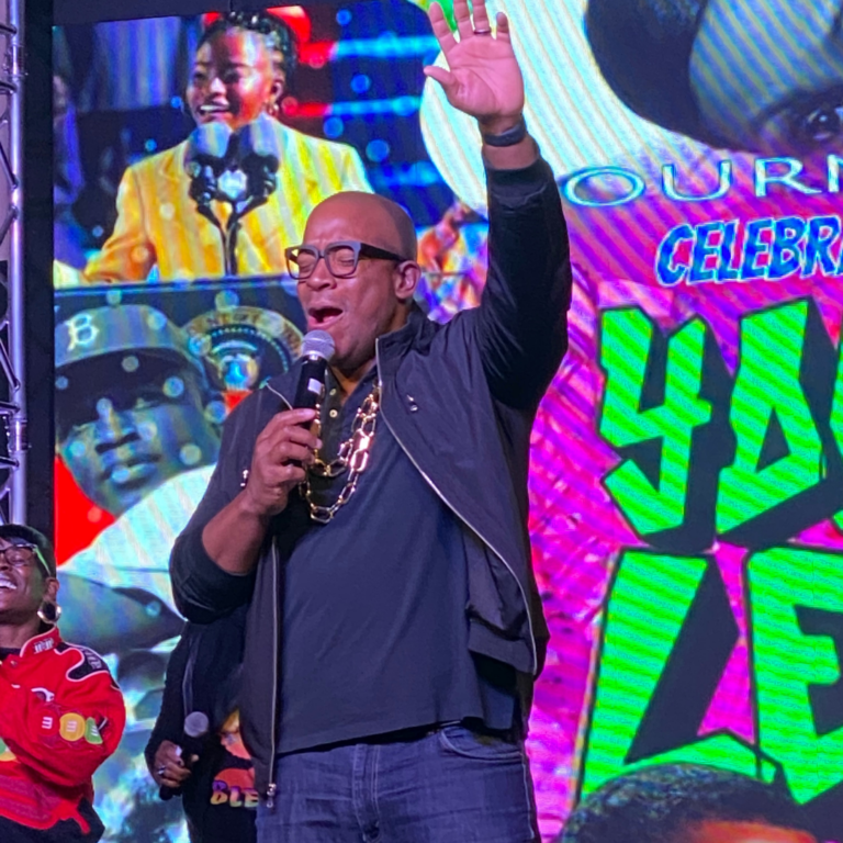 A man is standing in front of a large screen holding a microphone.