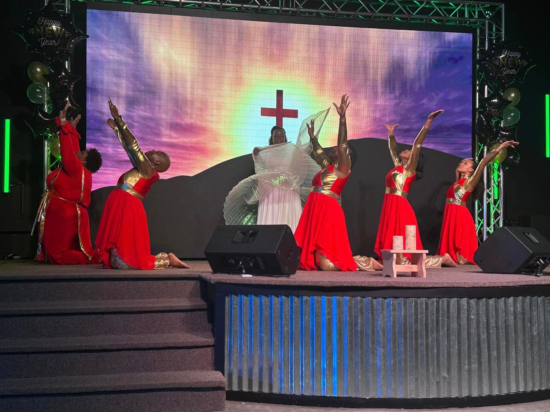 A group of women are dancing on a stage in front of a large screen.
