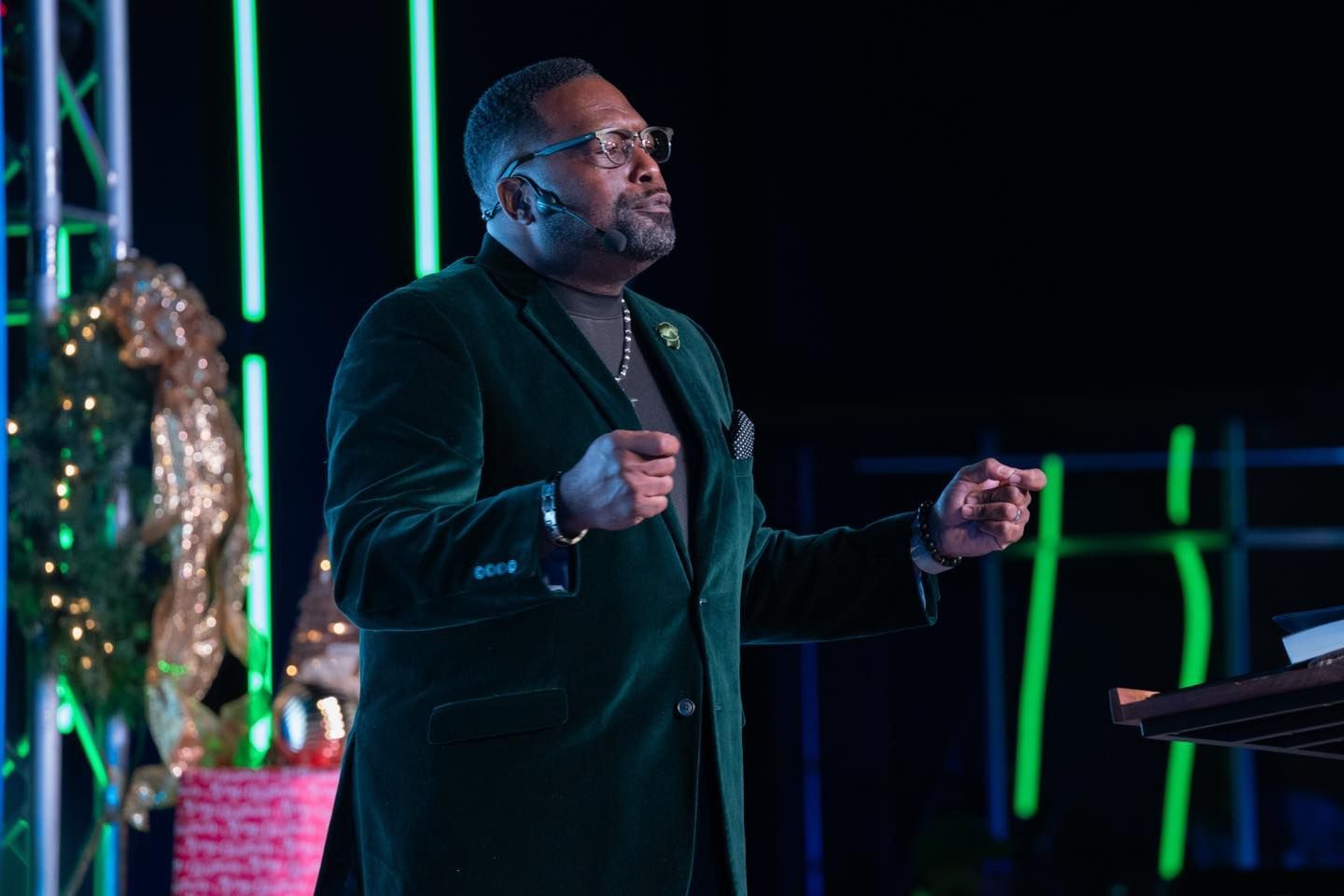 A man in a green suit is standing on a stage giving a speech.