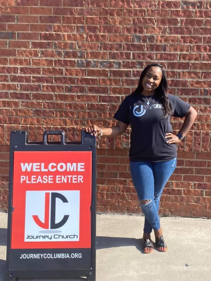 A woman standing next to a sign that says welcome please enter