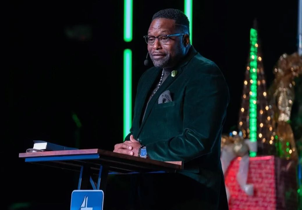 A man in a green suit is standing at a podium giving a speech.