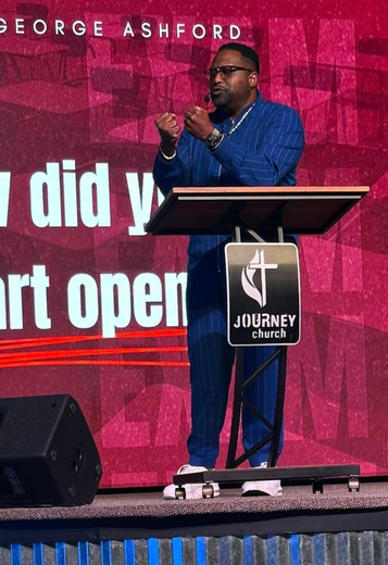 A man stands at a podium with a sign that says journey church